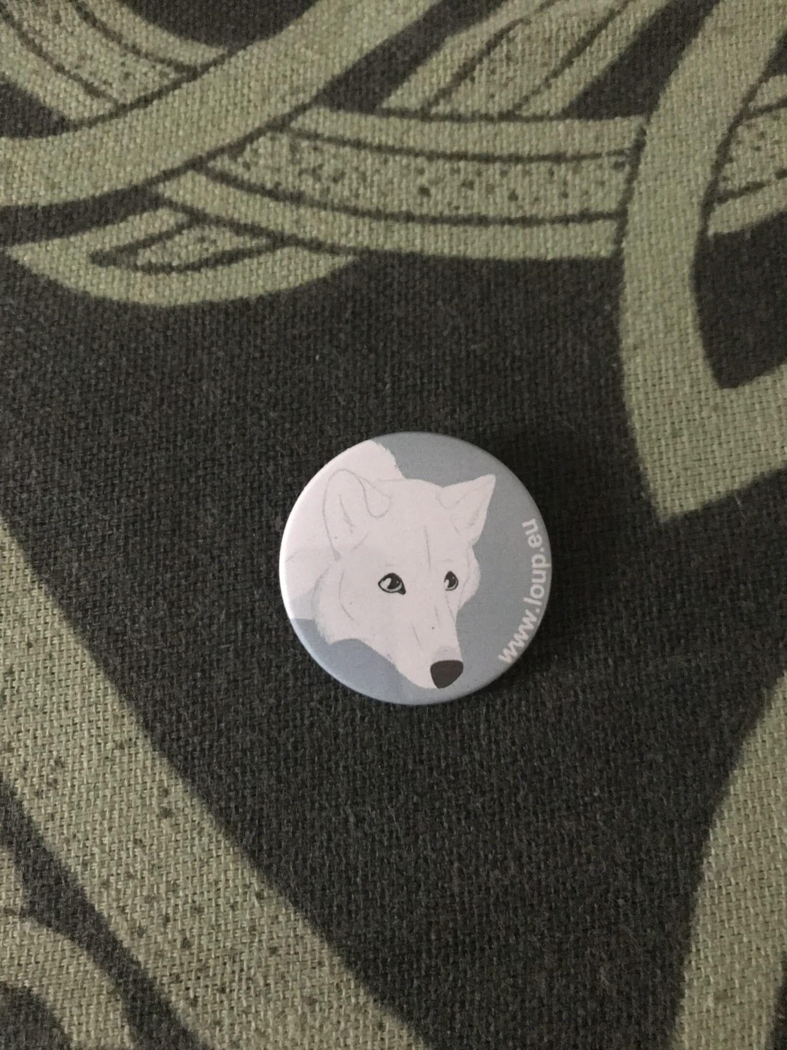 Photographie d'un badge représentant un dessin d'un loup blanc.
