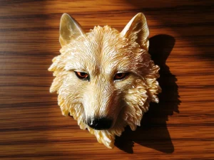 Magnet décoratif en relief représentant une tête de loup blanc sur une surface en bois.